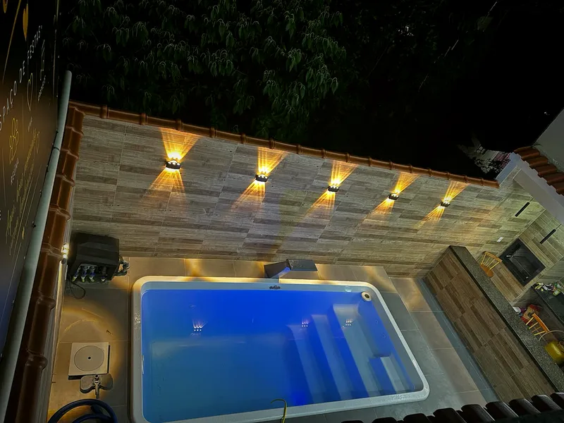 Piscina com cascata, luzes na parede e área gourmet ao lado